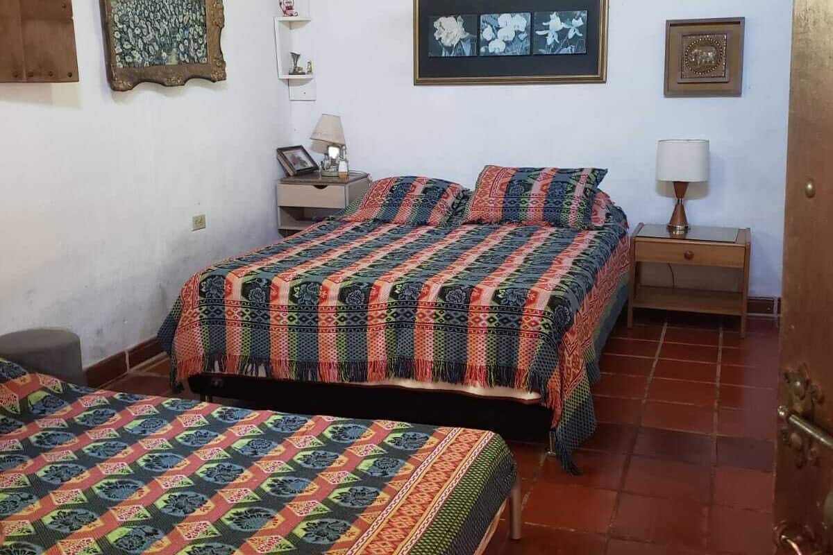 Una habitación con dos camas, techo de madera, lámpara colgante y una pared decorada con cuadros.