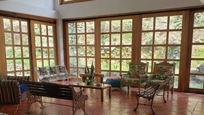 Habitación amplia con ventanas grandes, suelo de baldosas y diversas opciones de asientos, incluyendo un sofá, sillas y un banco.