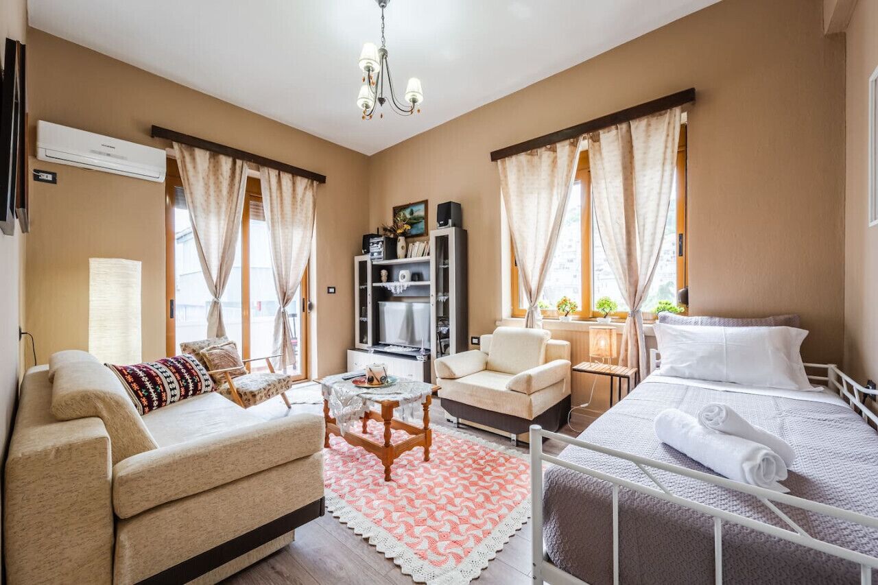 A hotel room with a bed, a sofa, a chair, a small table, and a TV.