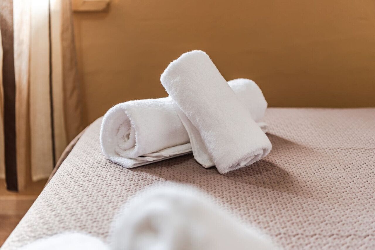 Une serviette blanche, soigneusement pliée, est posée sur un couvre-lit à motifs dans une chambre d’hôtel.