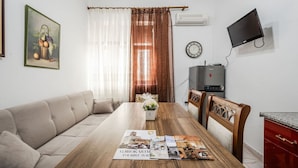 En stue med sofa, et træspisebord med magasiner, et fjernsyn og et ur på væggen.