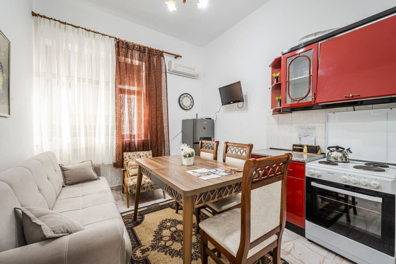 Un espace de vie compact comprenant un canapé, une table à manger, des chaises, une cuisine rouge avec une cuisinière et un téléviseur fixé au mur.