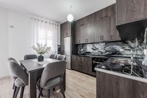 A modern kitchen with dark wood cabinets, a stainless steel sink, and a dining area with a table and chairs. - City Escape Apartment by PikHost (Shkodër)