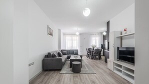 A modern living room with a grey sofa, a coffee table, and a TV on a stand. - City Escape Apartment by PikHost (Shkodër)