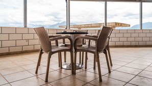A covered outdoor seating area with a table and chairs, large windows with a mountain view, and a tiled floor. - City Escape Apartment by PikHost (Shkodër)