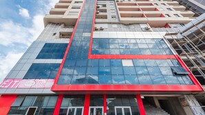 A multi-story building with a prominent red and blue facade, large glass windows, and a visible entrance with steps. - City Escape Apartment by PikHost (Shkodër)