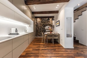A modern kitchen with a stone wall, wooden beams, and a dining area with a table and chairs.