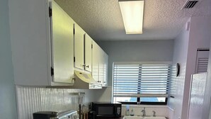 Pieni, käytännöllinen keittiö, jossa on valkoiset kaapit, puinen työtaso, mikroaaltouuni, kahvinkeitin ja pesuallas.