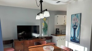Moderni ruokailutila, jossa on puinen pöytä, tuolit, televisio ja taideteoksia seinillä.