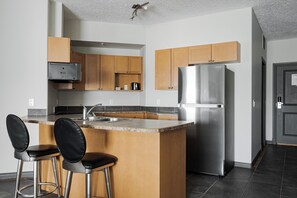 Une cuisine moderne dotée d’un îlot central, d’appareils électroménagers en acier inoxydable, de meubles en bois et de tabourets de bar noirs.