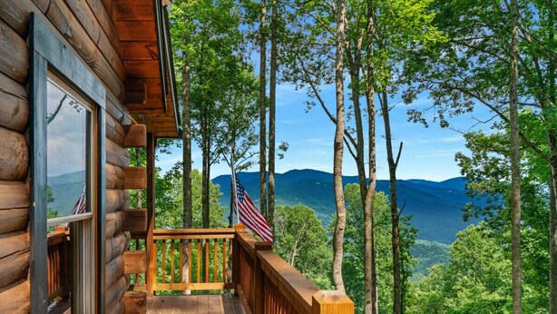 A wooden cabin with a deck, an American flag, and a view of mountains. - The Three Dog Night Cabin (Bryson City)