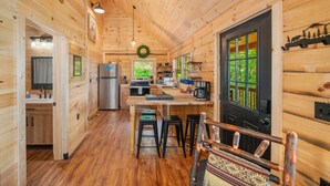 A wooden cabin interior with a kitchen, dining area, and a door with a view of greenery. - The Three Dog Night Cabin (Bryson City)