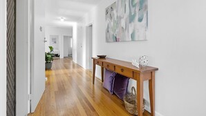Een hal met houten vloer, een console tafel met decoratieve objecten, en een groot abstract schilderij aan de muur.