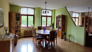 Un comedor con una mesa y sillas de madera, un radiador y una ventana con cortinas de encaje.