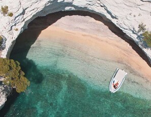 An aerial view of a beach with a boat anchored near a natural rock arch.