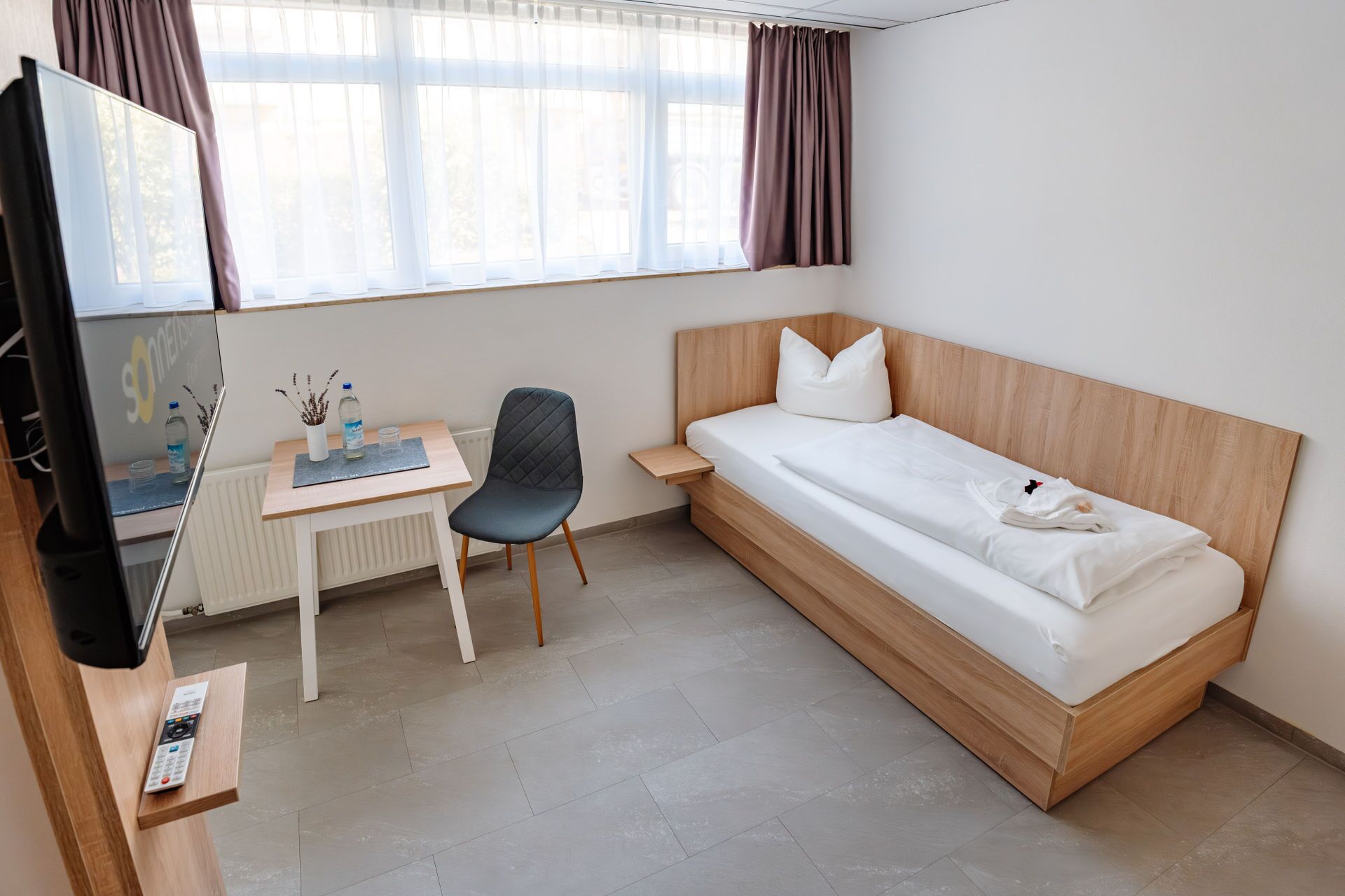 Una camera d'albergo con un letto, una scrivania con una sedia, una televisione e una finestra con tende.