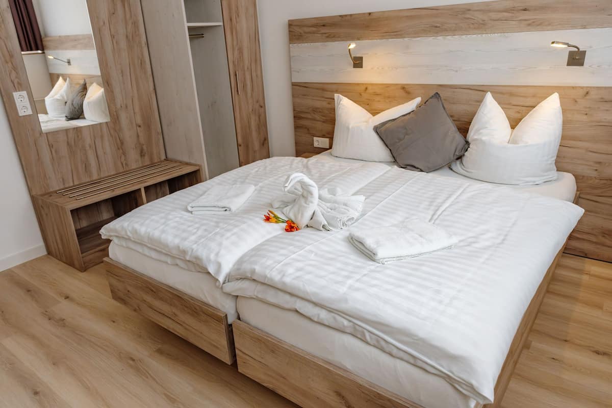 Un lit bien fait, avec du linge de lit blanc, une tête de lit en bois et une table de chevet avec une lampe.