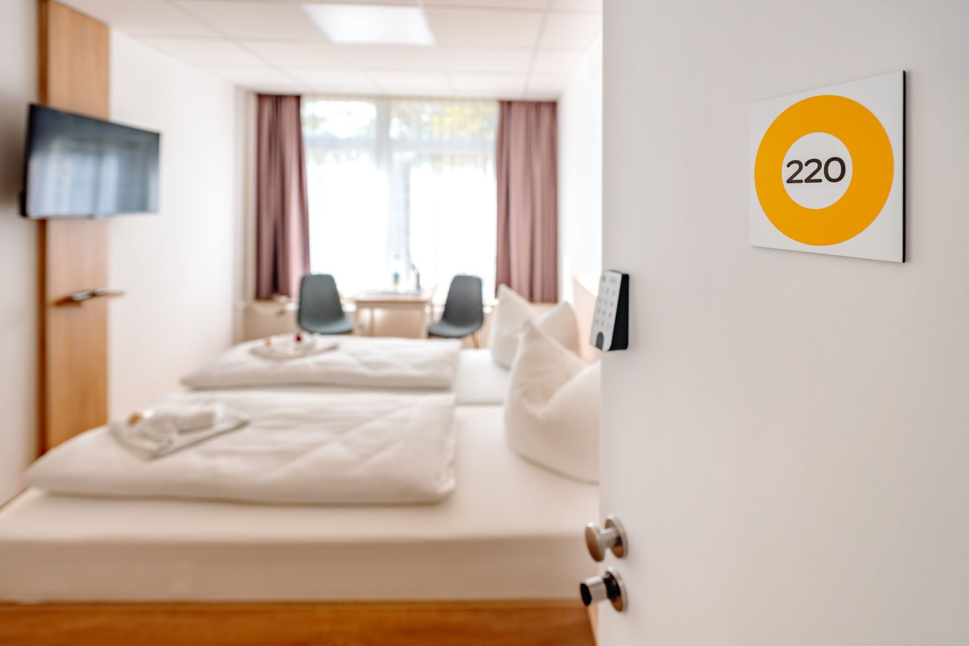 Une chambre d’hôtel avec deux lits, un téléviseur fixé au mur et une pancarte portant le numéro 220.