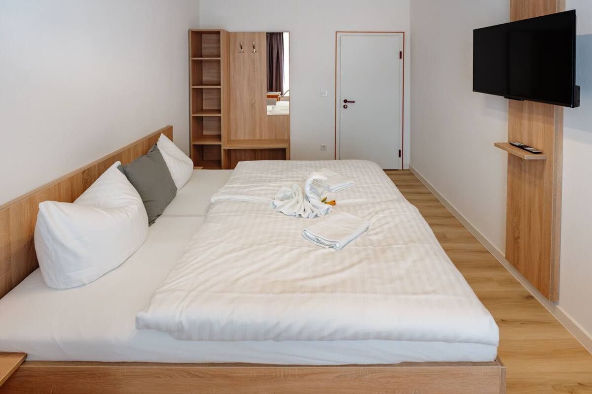 Une chambre d’hôtel avec un lit, une armoire en bois, un téléviseur fixé au mur et une porte.