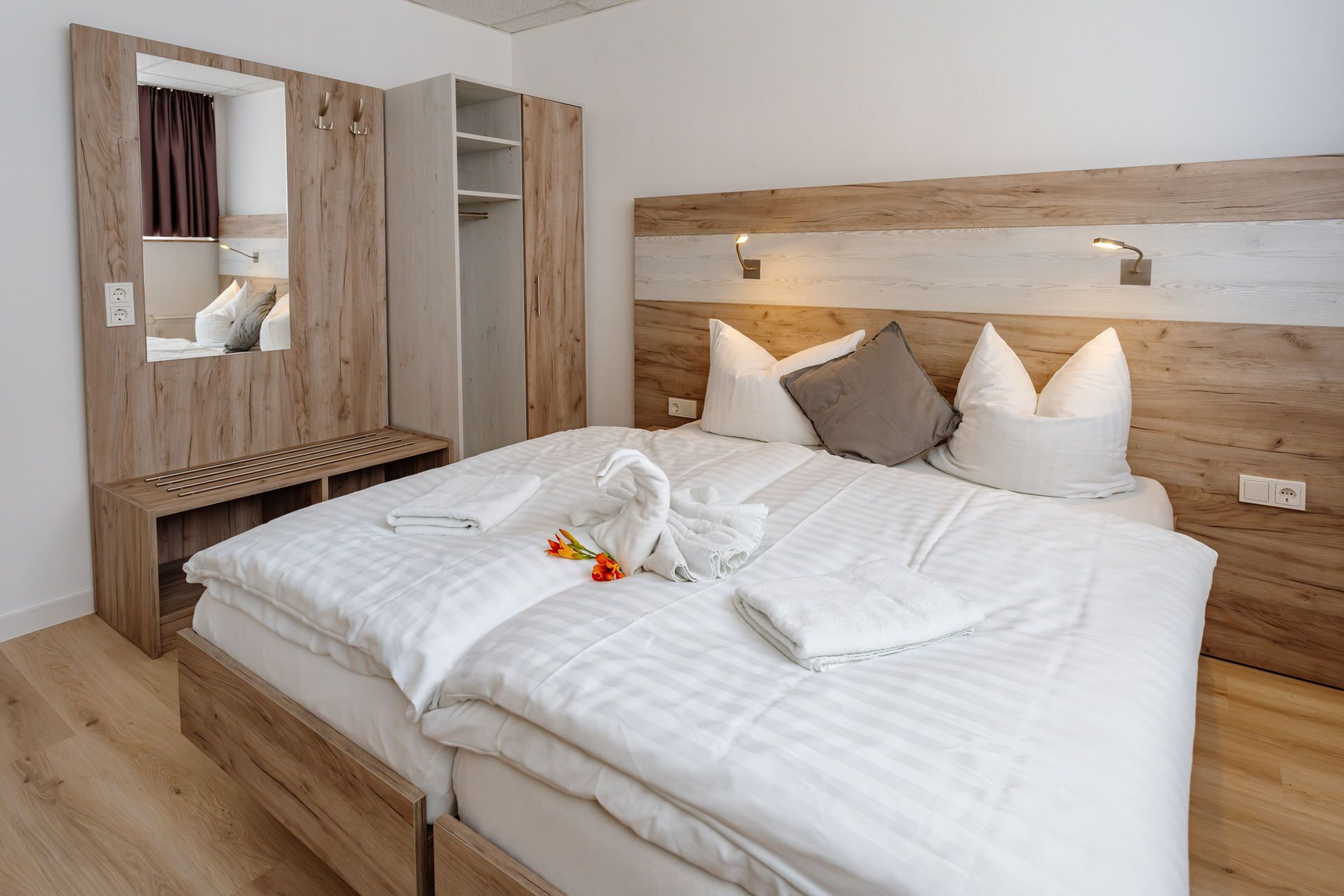 A neatly made bed with a wooden headboard, a bedside table, and a mirror with a curtain.