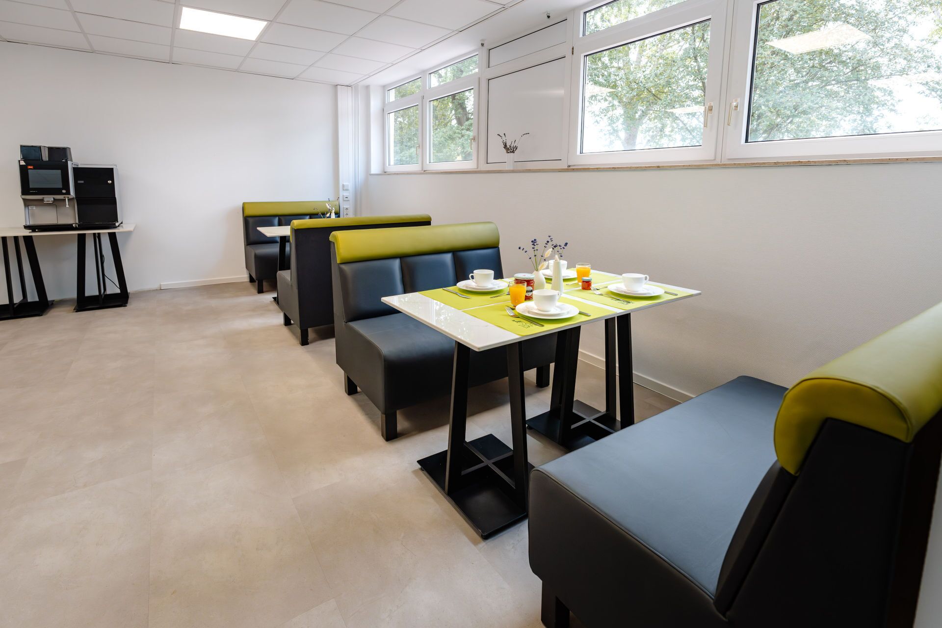 A dining area with booths and tables, equipped with chairs, a small TV, and a window with a view of trees.