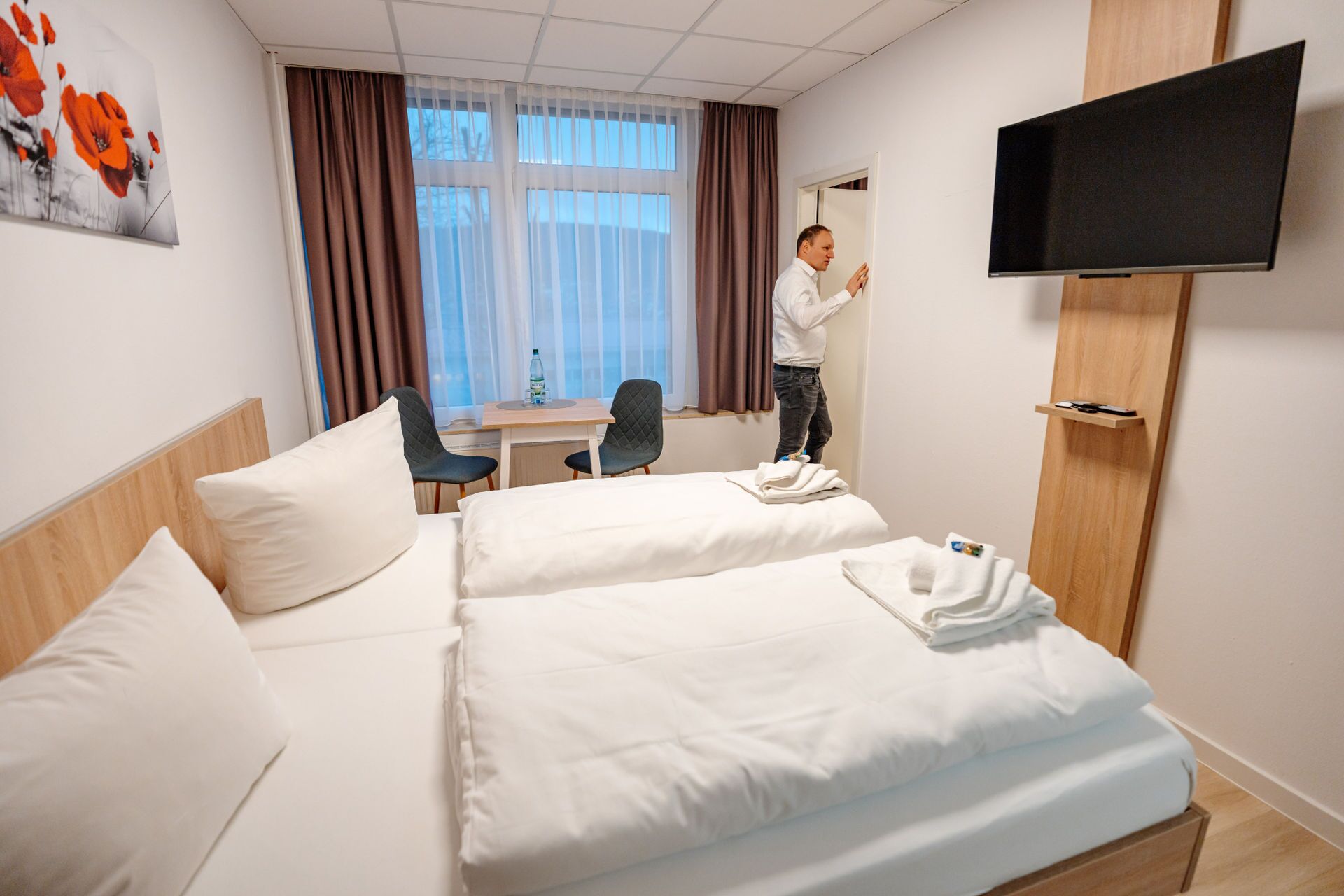 A hotel room with two beds, a desk, a chair, a TV, and a painting on the wall.