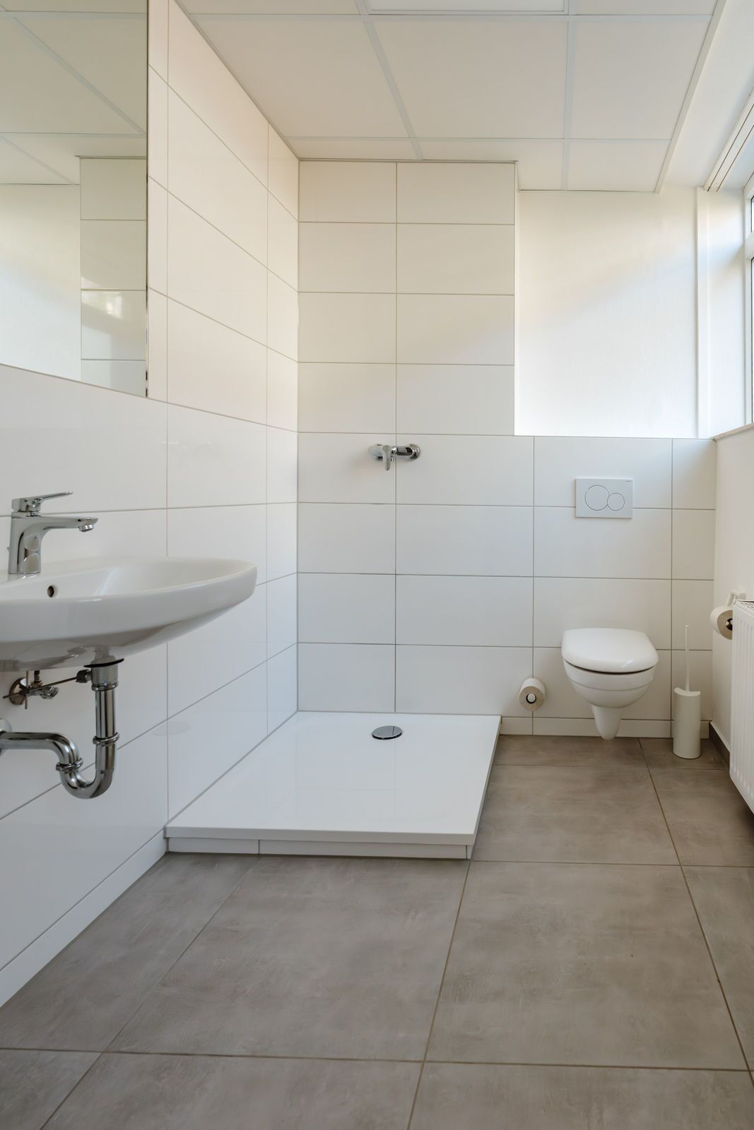 Un baño moderno con azulejos blancos, un lavabo, un inodoro y una zona de ducha.
