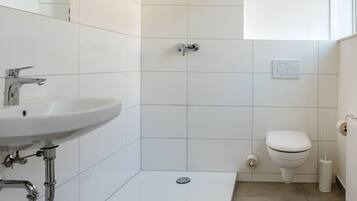 Un baño moderno con azulejos blancos, un lavabo, un inodoro y una zona de ducha.