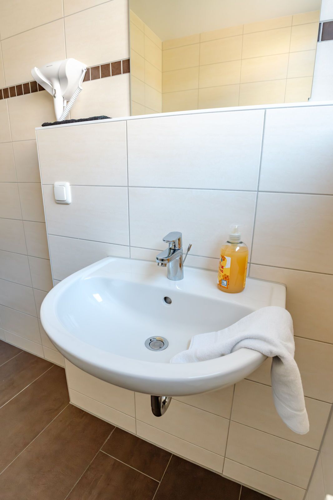 Un lavabo blanco con grifo cromado, un dispensador de jabón y una toalla colgada en la pared.