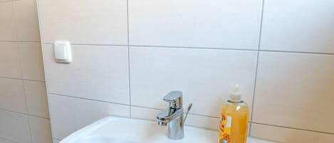 A white bathroom sink with a chrome faucet, a soap dispenser, and a towel hanging on the wall.