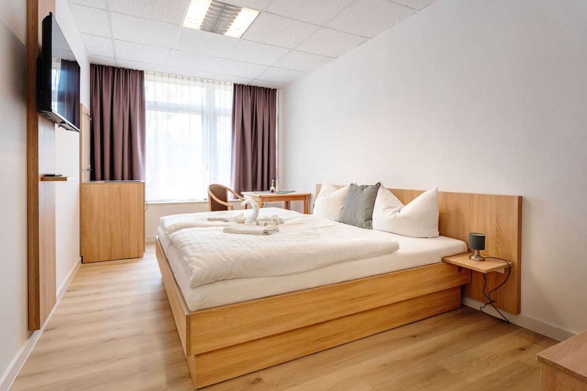 Une chambre d’hôtel moderne avec un lit en bois, un bureau, une chaise et un téléviseur fixé au mur.