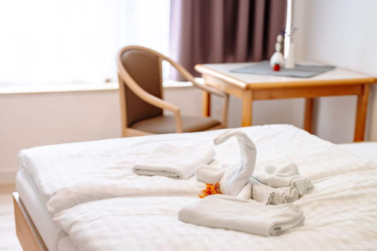 Un lit parfaitement fait, avec du linge de lit blanc et une serviette pliée en forme de cygne.