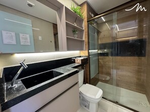 A modern bathroom with a glass shower enclosure, a white toilet, and a black countertop with a sink. - COMPACTO TAMBAÚ (João Pessoa)