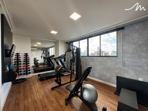 A gym with exercise equipment, a large window, and a city view. - COMPACTO TAMBAÚ (João Pessoa)