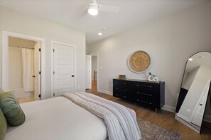 A bedroom with a bed, a dresser, a mirror, and a ceiling fan.