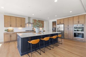 Una cocina moderna con armarios de madera, una isla grande con taburetes de bar, electrodomésticos de acero inoxidable e iluminación empotrada en el techo.