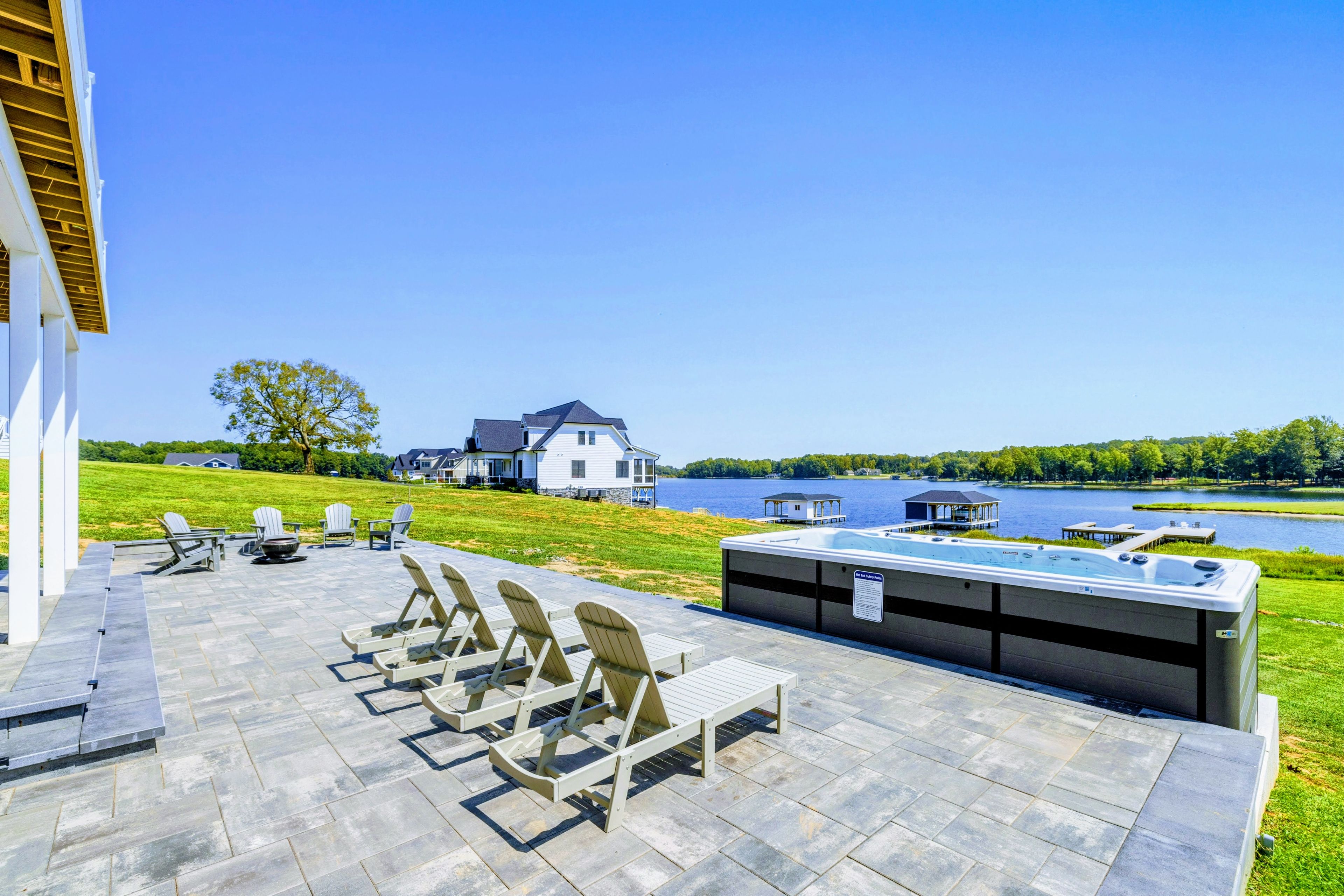 A patio with outdoor seating and a hot tub overlooking a lake.