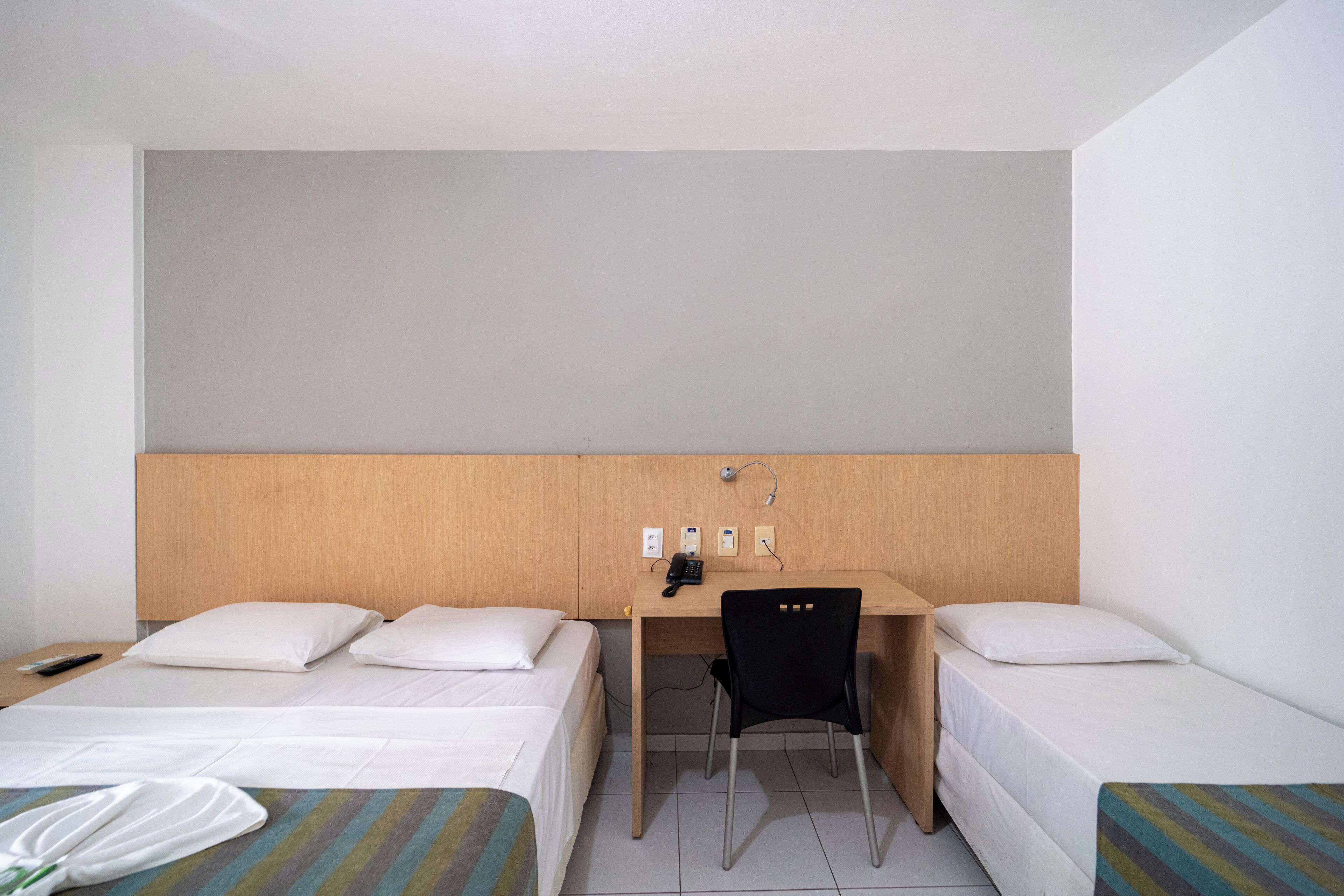 A hotel room with two beds, a desk with a chair, a telephone, and a remote control on the left bed.