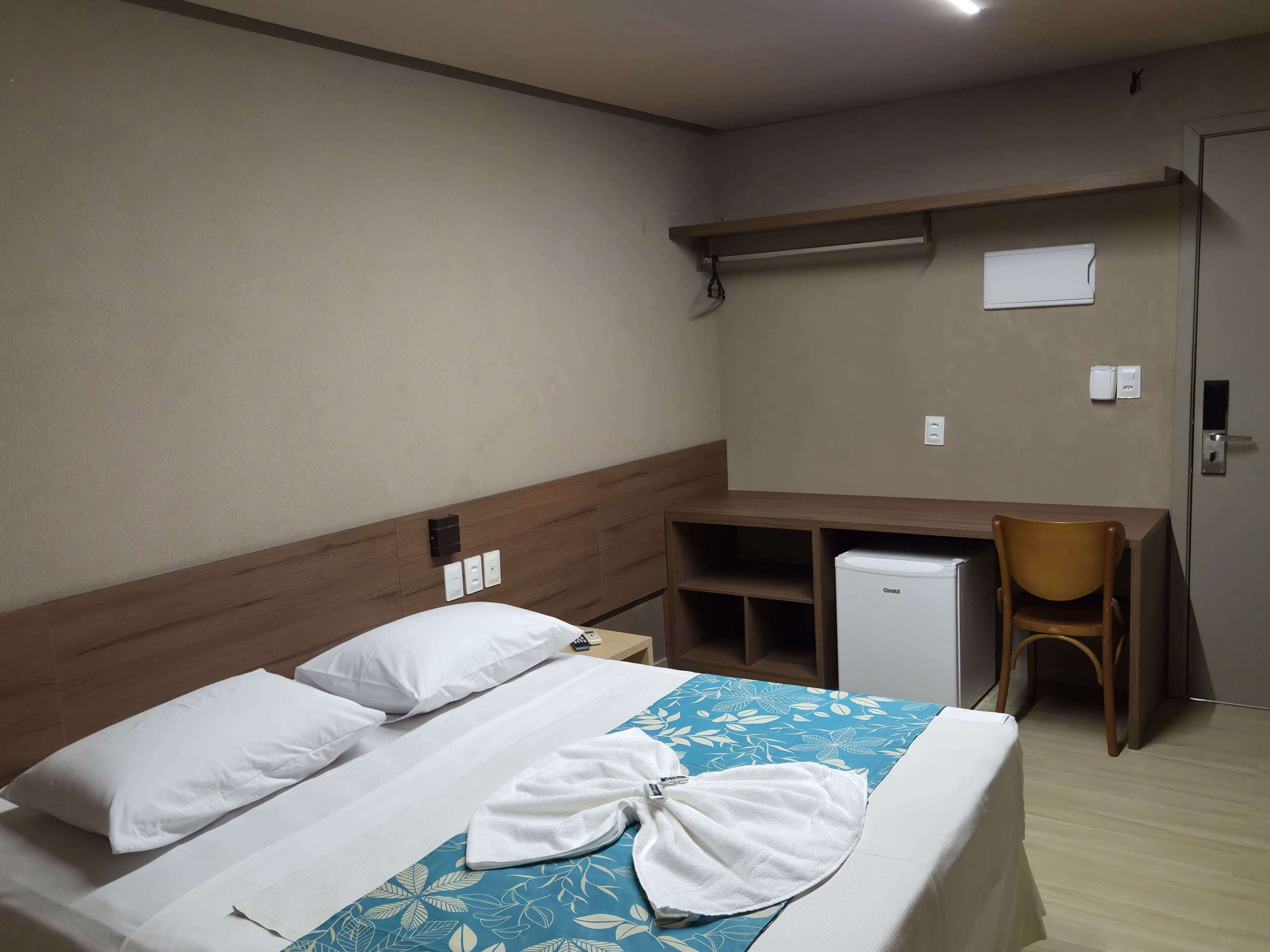 Habitación de hotel con cama, escritorio, silla y un refrigerador pequeño.
