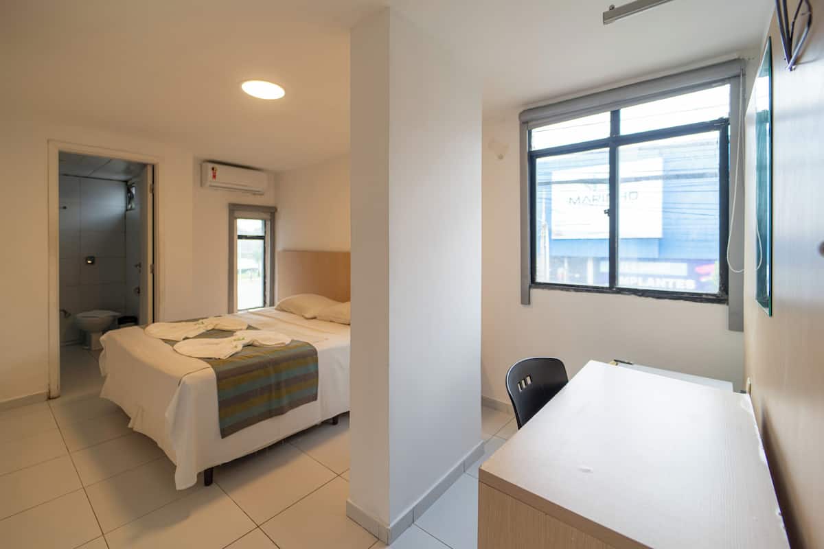 Hotelkamer met een bed, een bureau, een stoel, een raam met uitzicht op een gebouw en een airconditioning.