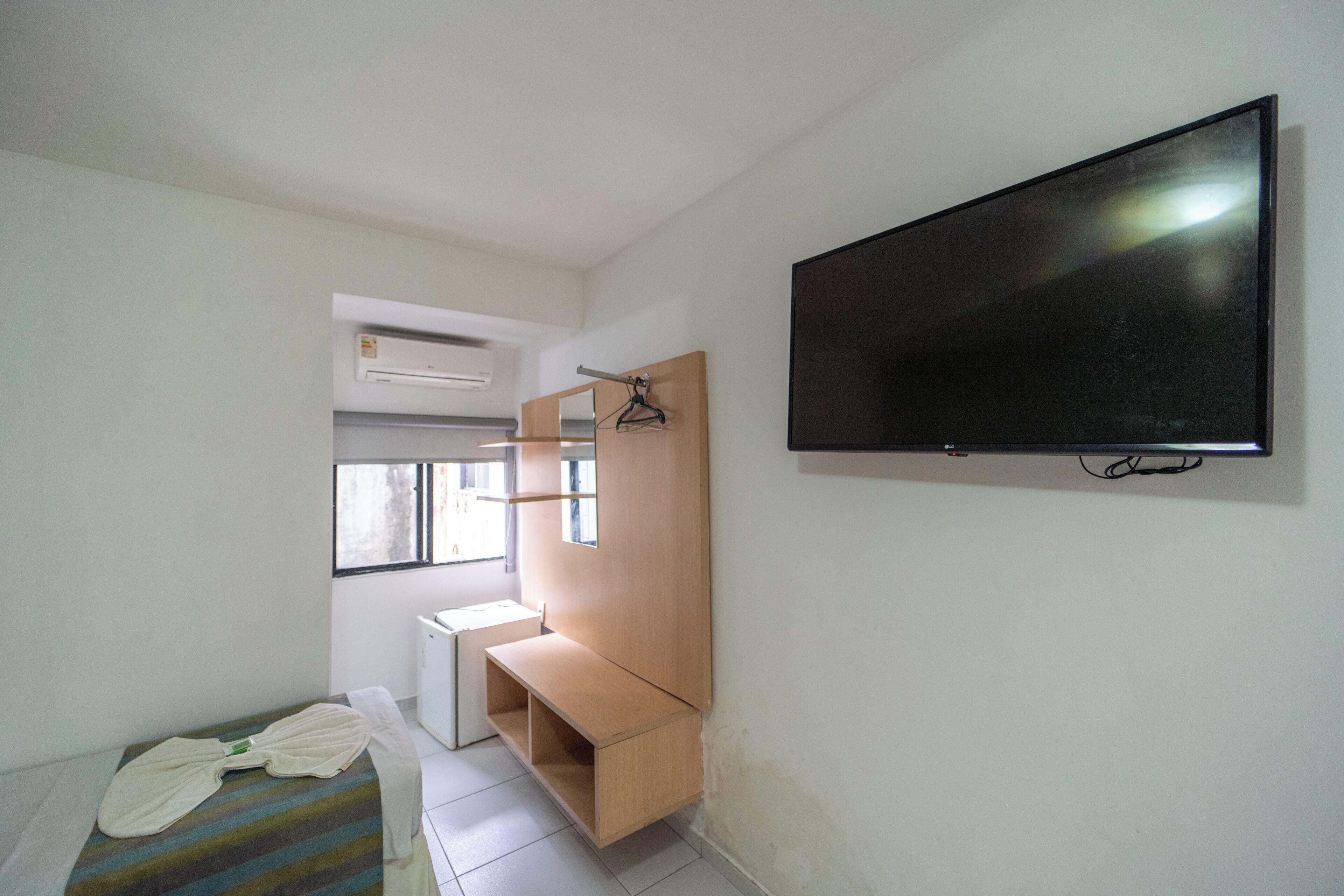 A room with a bed, a TV mounted on the wall, a wooden cabinet, and a window.