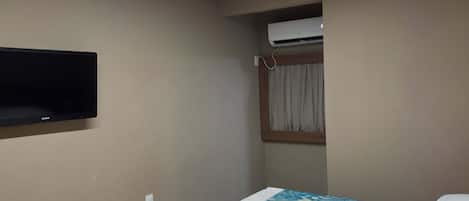Habitación de hotel con cama, televisor de pantalla plana montado en la pared, aire acondicionado y ventana con cortinas.