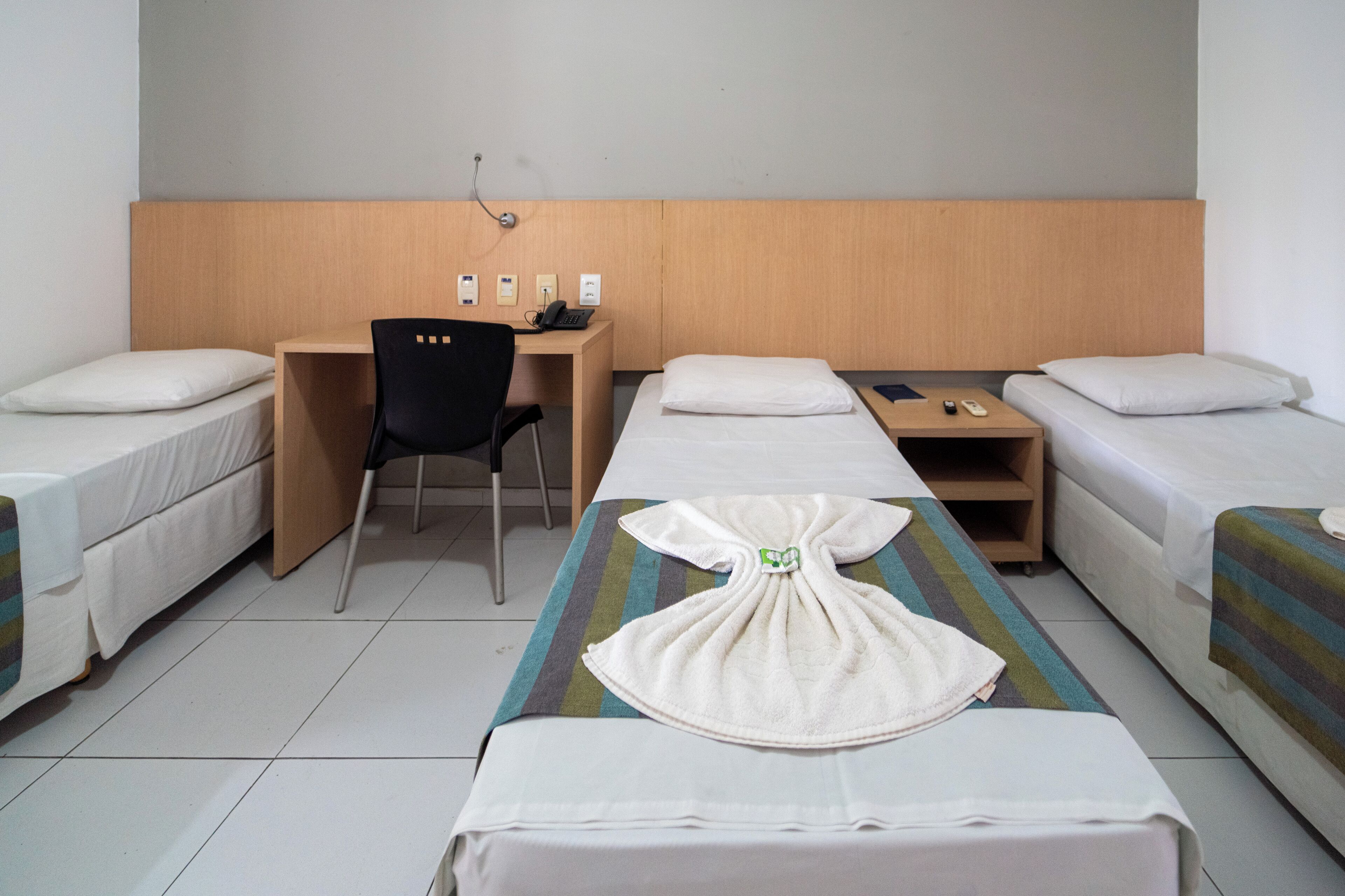 A hotel room with two single beds, a desk with a chair, a small table, and a wall-mounted phone.