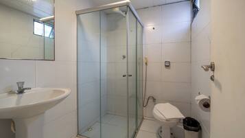Un baño con ducha envuelta en vidrio, un lavamanos, un inodoro y un cubo de basura.