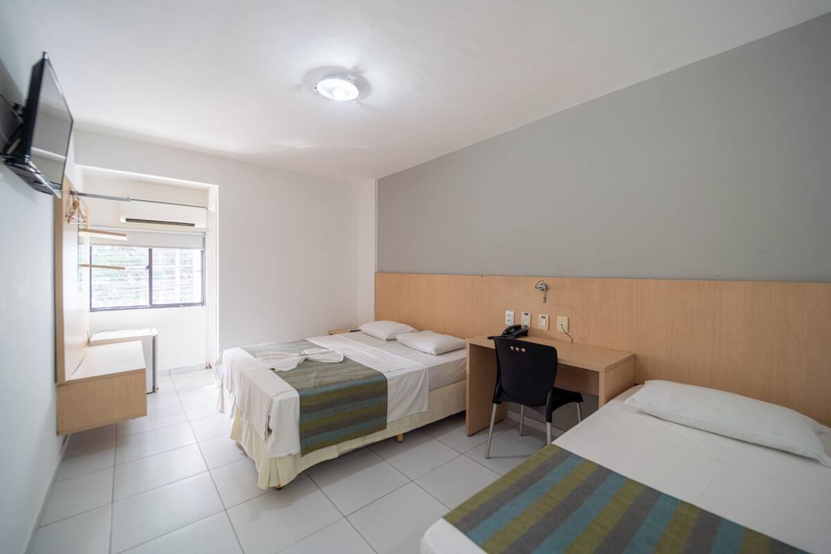 Hotelkamer met twee bedden, een bureau, een stoel, een aan de muur bevestigde televisie en een raam voor natuurlijk licht.