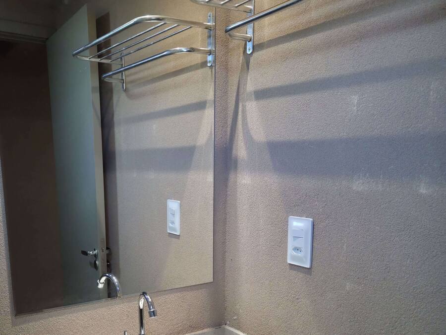 Un baño con lavamanos, espejo, toallero y dos enchufes en la pared.