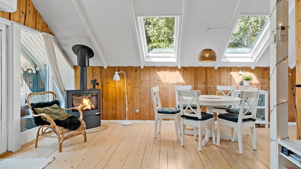 Une pièce chaleureuse avec un poêle à bois, une table à manger avec des chaises et une grande fenêtre.
