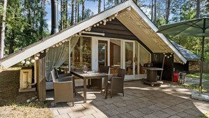 Une terrasse extérieure accueillante, avec une table et des chaises pour les repas, un barbecue et un espace salon couvert agrémenté de rideaux.