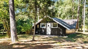Une petite cabane avec un toit en pente, une porte et une fenêtre. Il y a une table et deux chaises à l’extérieur.
