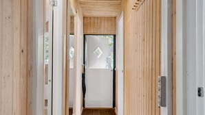 Un couloir étroit en bois, avec une porte au bout, une petite fenêtre et un interphone.